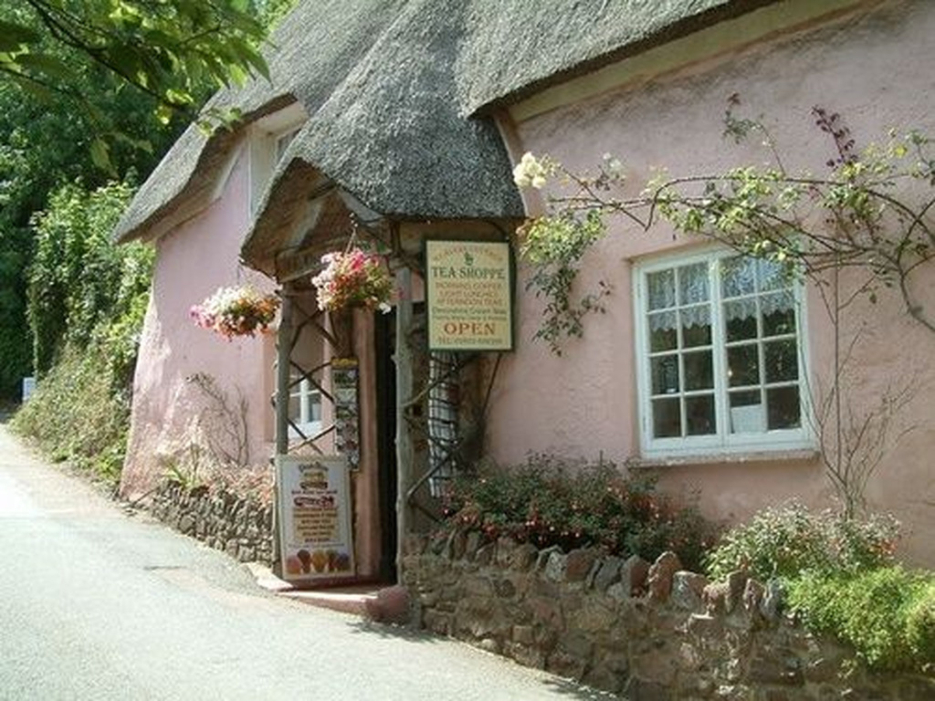AI caption: a pink thatched cottage with flowers on the front, a cottage